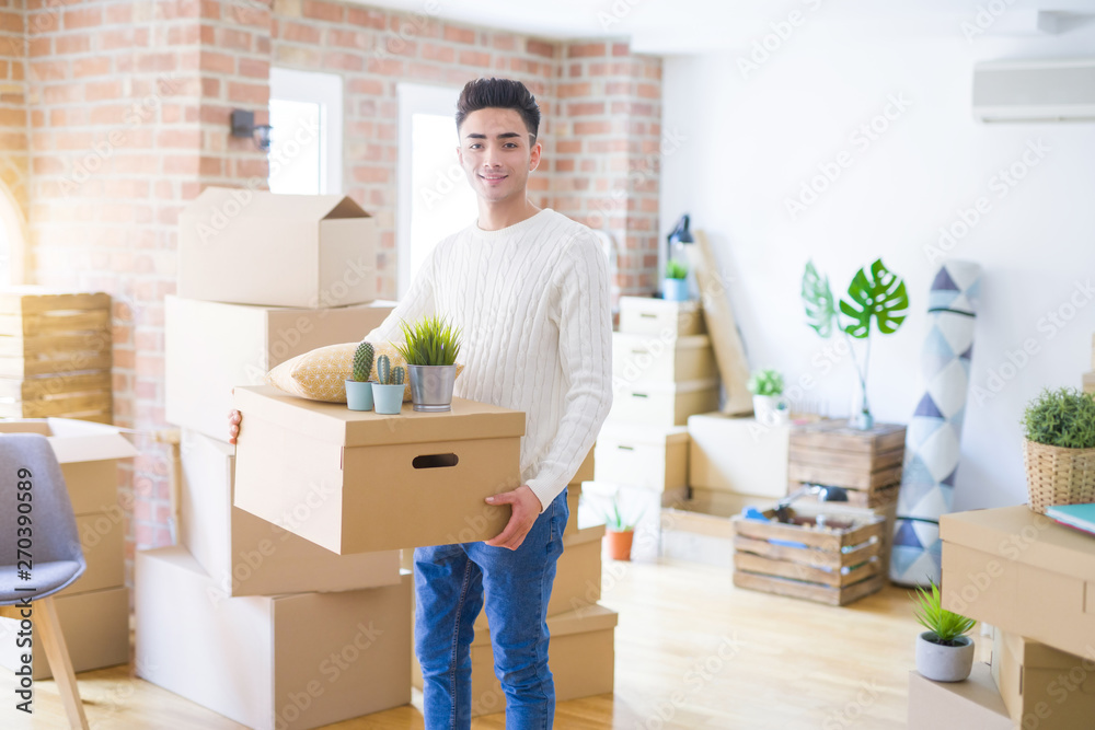 Young man smiling holdig cardboard box, happy moving to a new house Young man smiling holdig cardboard box, happy moving to a new house
