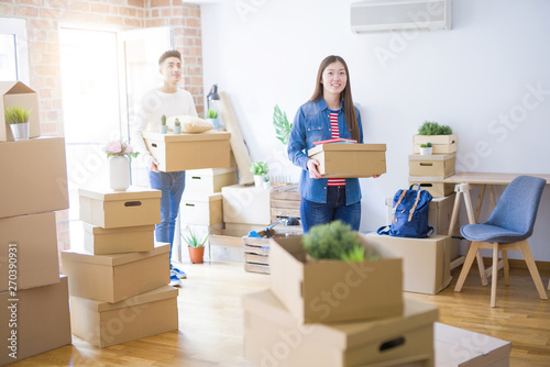 Beautiful young asian couple looking happy holding cardboard boxes, smiling excited moving to a new home