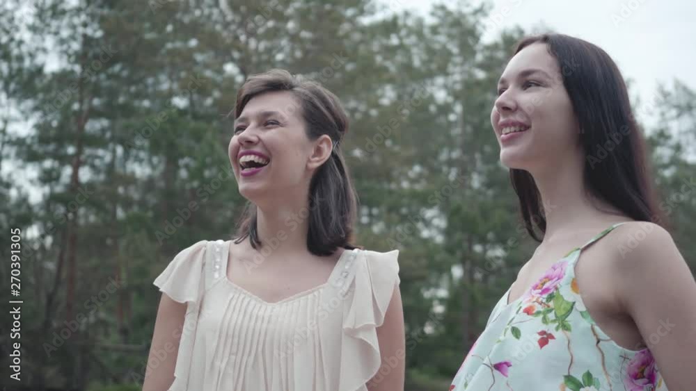 Portrait two cute smilling young women wear summer dresses standing in the top of rock and looking at amazing view of nature. Pretty girls walk outside the city. Adorable girlfriends outdoors. Portrait two cute smilling young women wear summer dresses standing in the top of rock and looking at amazing view of nature. Pretty girls walk outside the city. Adorable girlfriends outdoors.