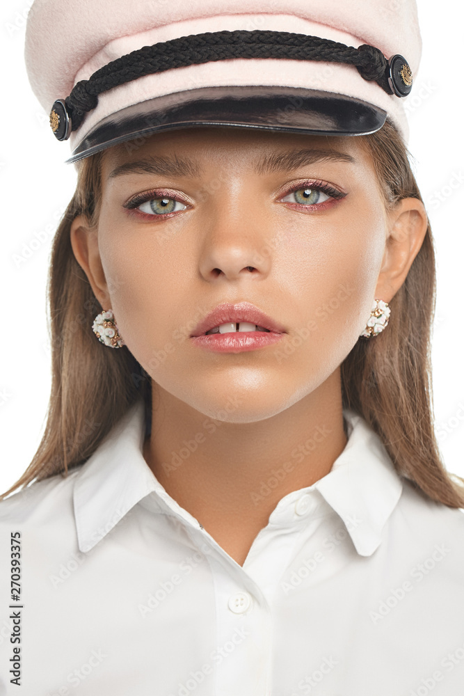 Portrait of girl with green eyes, wearing forage cap, tilting her head against white background. The lady is wearing massive earrings, adorned with shiny crystals and snow-white floral application. Portrait of girl with green eyes, wearing forage cap, tilting her head against white background. The lady is wearing massive earrings, adorned with shiny crystals and snow-white floral application.