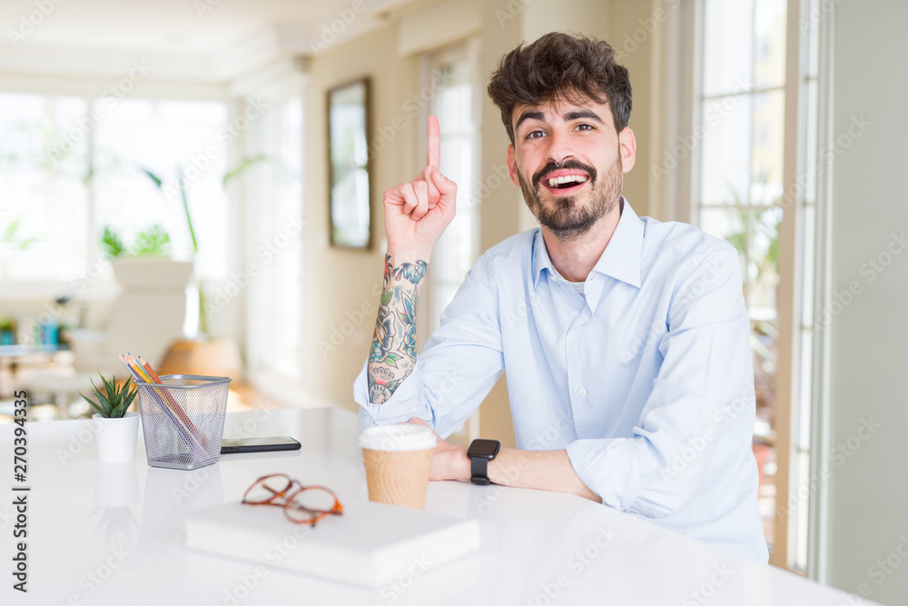 Young business man working pointing finger up with successful idea. Exited and happy. Number one.