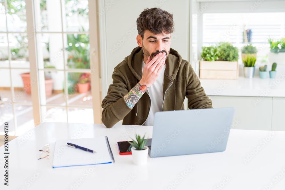 Young student man using computer laptop and notebook cover mouth with hand shocked with shame for mistake, expression of fear, scared in silence, secret concept Young student man using computer laptop and notebook cover mouth with hand shocked with shame for mistake, expression of fear, scared in silence, secret concept