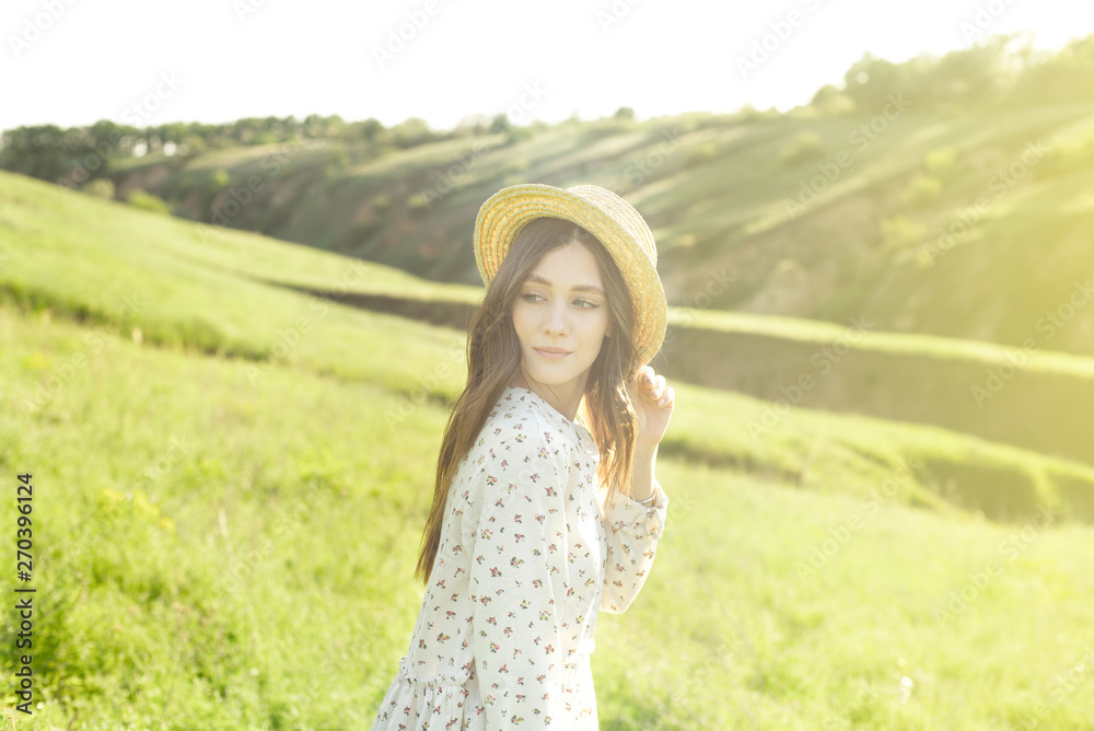 Beautiful sensual brunette in dress and hat standing with eyes closed in nature in bright back lit.