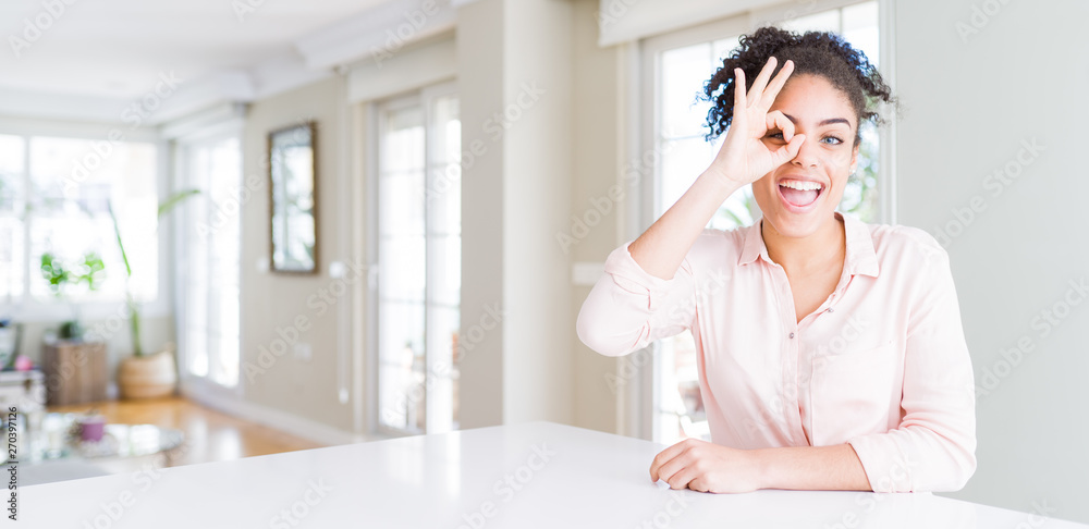 Wide angle of beautiful african american woman with afro hair doing ok gesture with hand smiling, eye looking through fingers with happy face. Wide angle of beautiful african american woman with afro hair doing ok gesture with hand smiling, eye looking through fingers with happy face.