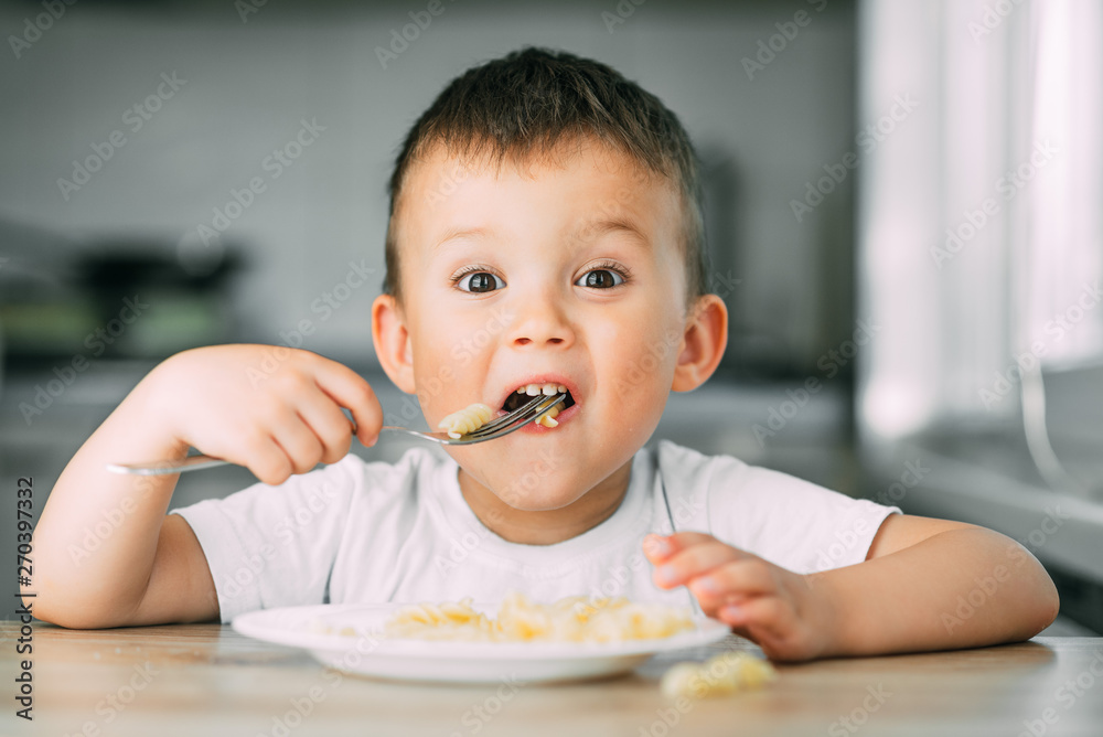 a little boy eats pasta in the form of a spiral in the afternoon in the kitchen on their own a little boy eats pasta in the form of a spiral in the afternoon in the kitchen on their own