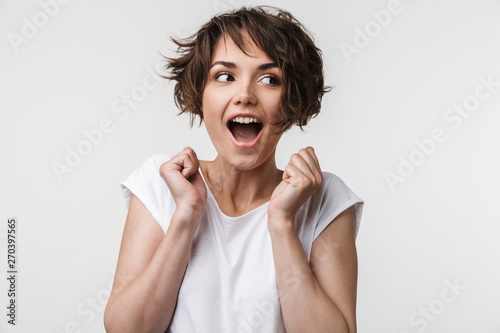 Portrait of joyous woman with short brown hair in basic t-shirt rejoicing and clenching fists