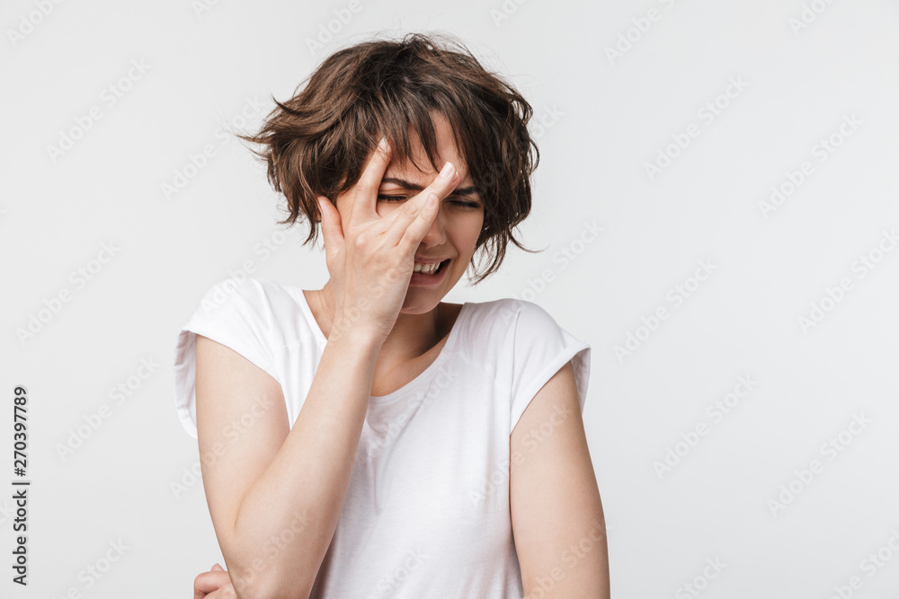 Portrait of scared woman with short brown hair in basic t-shirt frowning and covering her eyes Portrait of scared woman with short brown hair in basic t-shirt frowning and covering her eyes