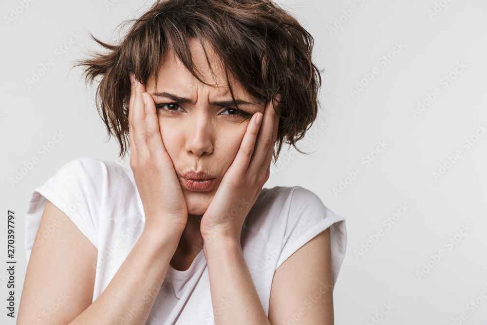 Photo of confused woman with short brown hair in basic t-shirt keeping hands over her face and frowning at camera Photo of confused woman with short brown hair in basic t-shirt keeping hands over her face and frowning at camera
