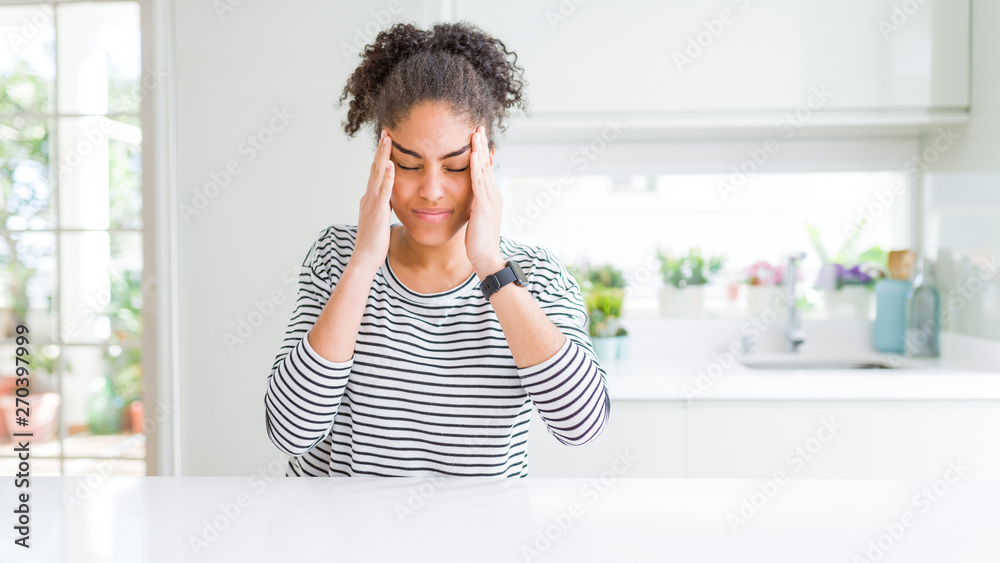 Beautiful african american woman with afro hair wearing casual striped sweater with hand on headache because stress. Suffering migraine. Beautiful african american woman with afro hair wearing casual striped sweater with hand on headache because stress. Suffering migraine.