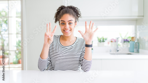 Beautiful african american woman with afro hair wearing casual striped sweater showing and pointing up with fingers number eight while smiling confident and happy.