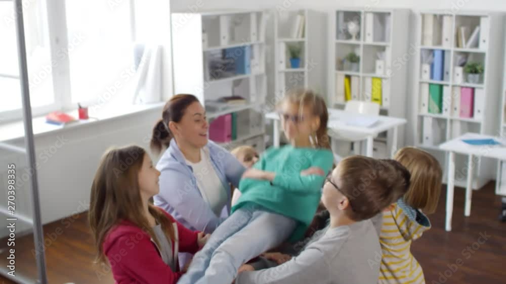 Medium shot of smiling 12-year-old girl standing high up with closed eyes in sunny school counselor’s office, then falling backwards onto friends’ arms and climbing back up looking pleased Medium shot of smiling 12-year-old girl standing high up with closed eyes in sunny school counselor’s office, then falling backwards onto friends’ arms and climbing back up looking pleased