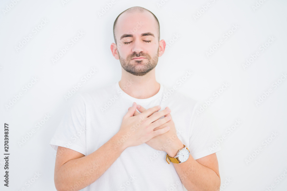 Young bald man over white isolated background smiling with hands on chest with closed eyes and grateful gesture on face. Health concept. Young bald man over white isolated background smiling with hands on chest with closed eyes and grateful gesture on face. Health concept.
