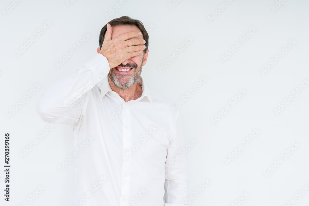 Elegant senior man over isolated background smiling and laughing with hand on face covering eyes for surprise. Blind concept. Elegant senior man over isolated background smiling and laughing with hand on face covering eyes for surprise. Blind concept.
