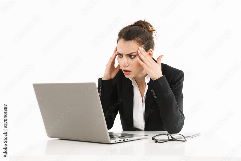 Photo of tense female worker businesswoman dressed in formal wear sitting at desk and working on laptop in office Photo of tense female worker businesswoman dressed in formal wear sitting at desk and working on laptop in office