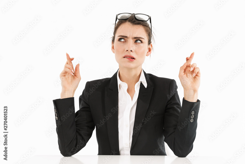 Photo of confident female worker businesswoman dressed in formal wear keeping fingers crossed while working and sitting at desk in office Photo of confident female worker businesswoman dressed in formal wear keeping fingers crossed while working and sitting at desk in office