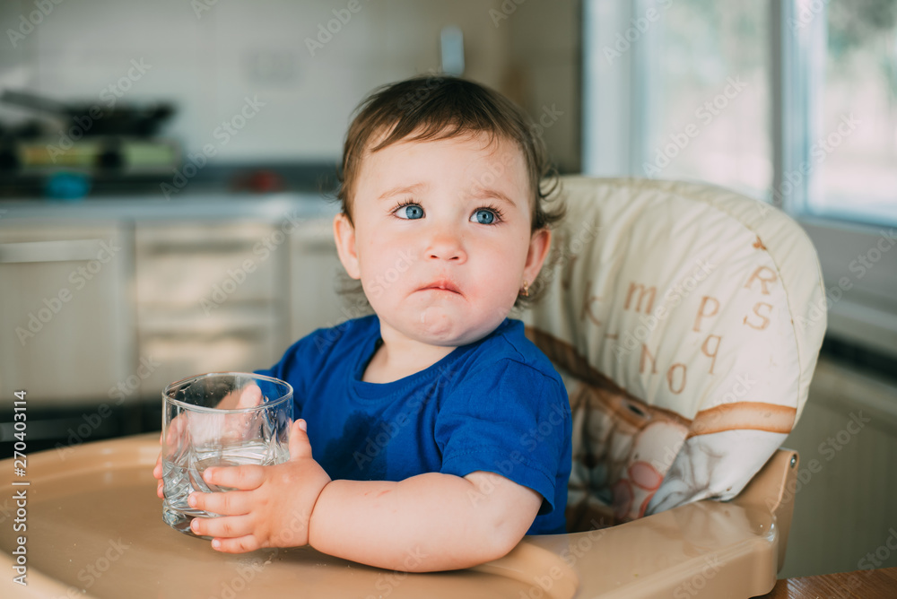 A little girl in the kitchen in the afternoon in a high chair drinking water from a glass glass A little girl in the kitchen in the afternoon in a high chair drinking water from a glass glass