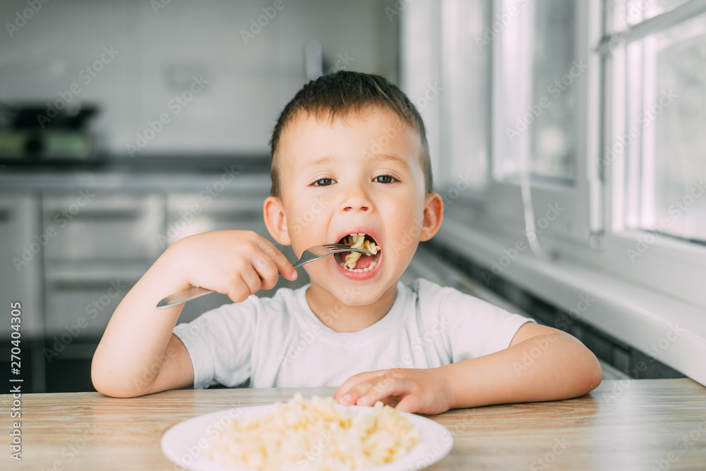 little boy eats pasta in the form of a spiral in the afternoon in the kitchen on their own little boy eats pasta in the form of a spiral in the afternoon in the kitchen on their own
