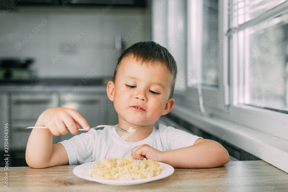 little boy eats pasta in the form of a spiral in the afternoon in the kitchen on their own little boy eats pasta in the form of a spiral in the afternoon in the kitchen on their own