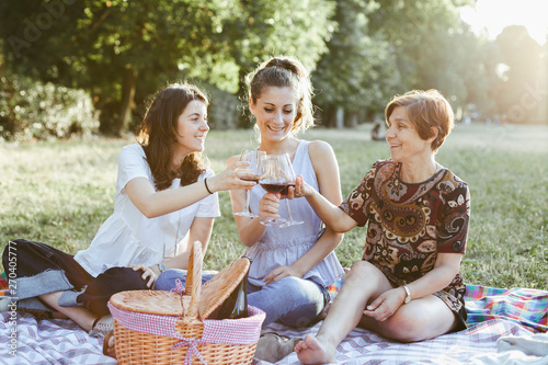 Mother and two daughters make picnic with toast in a park at sunset during summer
