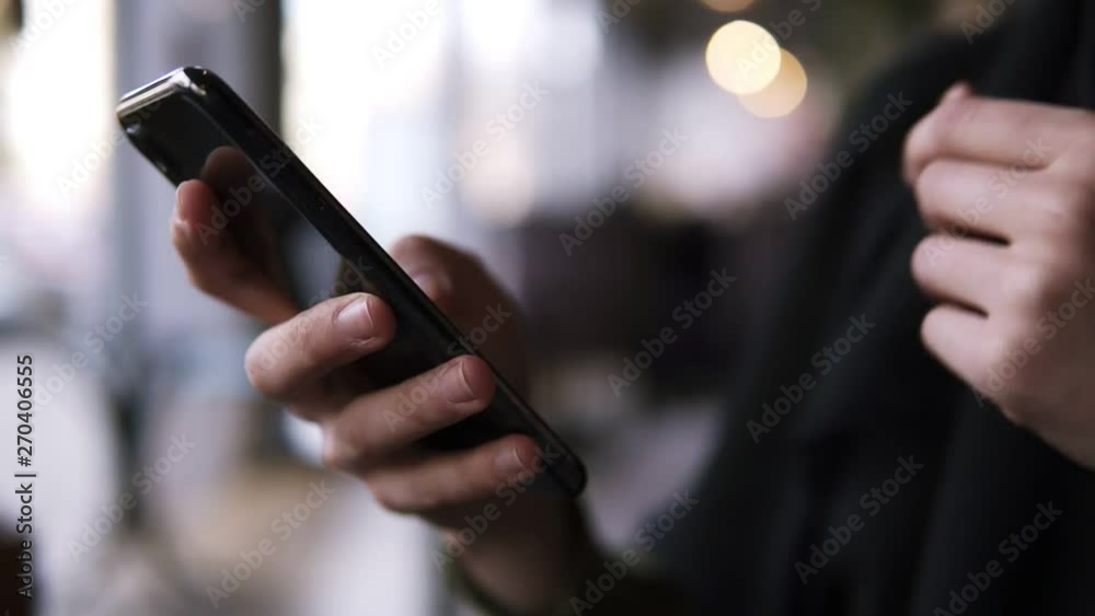 Close up of female's hands holding smartphone with fingers on a touchscreen. Woman browsing internet on a mobile phone. Slow motion. Blurred background