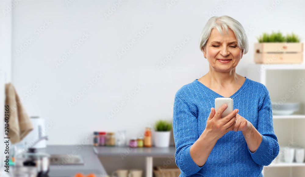 technology and old people concept - smiling senior woman using smartphone over kitchen background technology and old people concept - smiling senior woman using smartphone over kitchen background