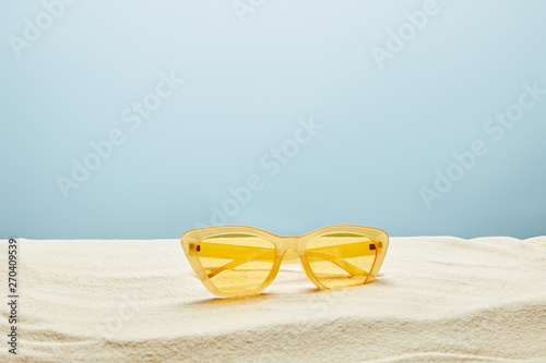 yellow stylish sunglasses on sand on blue background