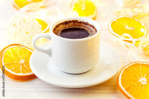 Romantic breakfast. A cup of black coffee and orange slices on a background of glowing lanterns. Postcard Design