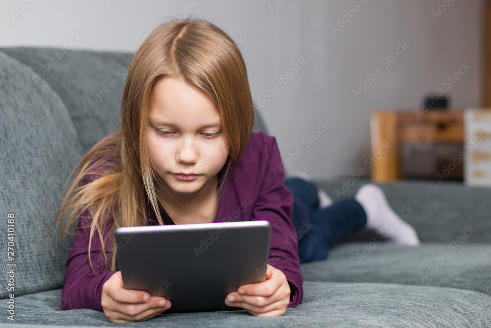 Portrait of a girl lying on the sofa and looking at a tablet PC in her hands