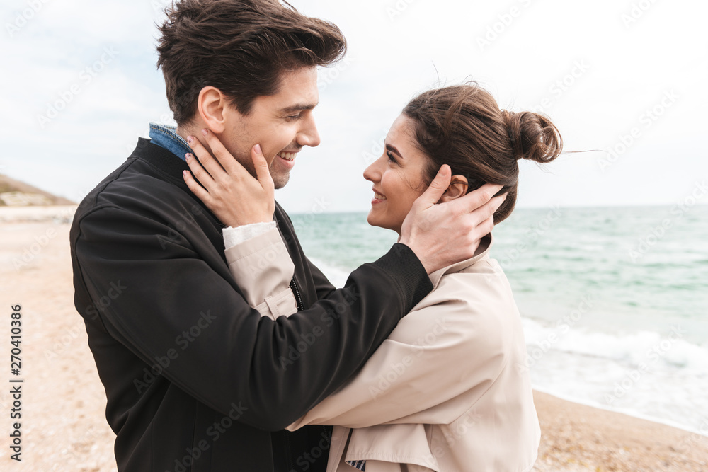 Happy lovely young couple wearing coats walking at the beach Happy lovely young couple wearing coats walking at the beach