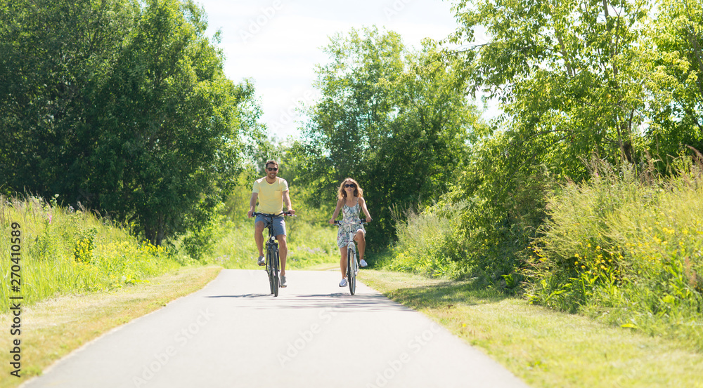 Fototapeta premium people, leisure and lifestyle concept - happy young couple riding bicycles along road in summer