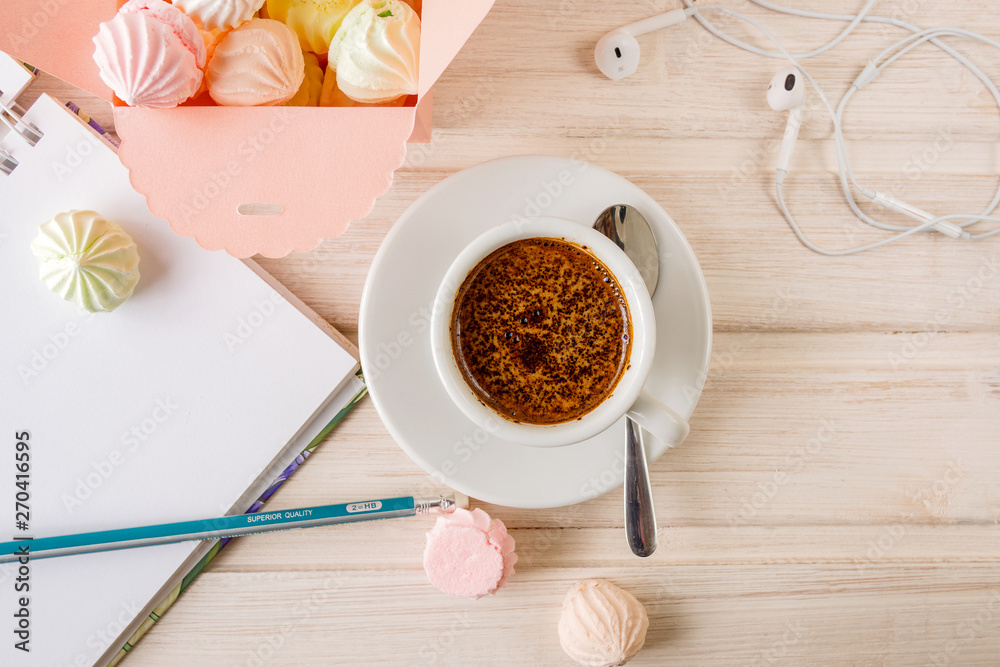 Morning coffee with a notebook and a pencil, with a box filled with small meringues, headphones on a wooden light background.Топ view. Morning coffee with a notebook and a pencil, with a box filled with small meringues, headphones on a wooden light background.Топ view.