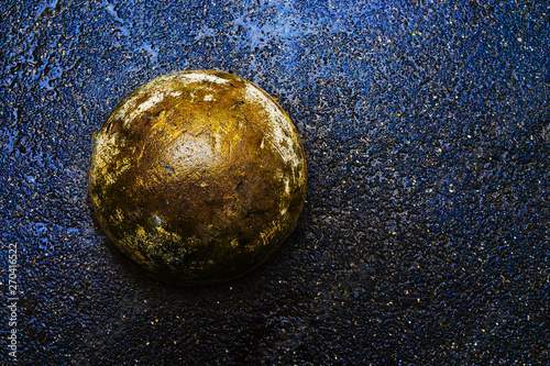 Golden concrete ball on wet dark asphalt. Abstract background.