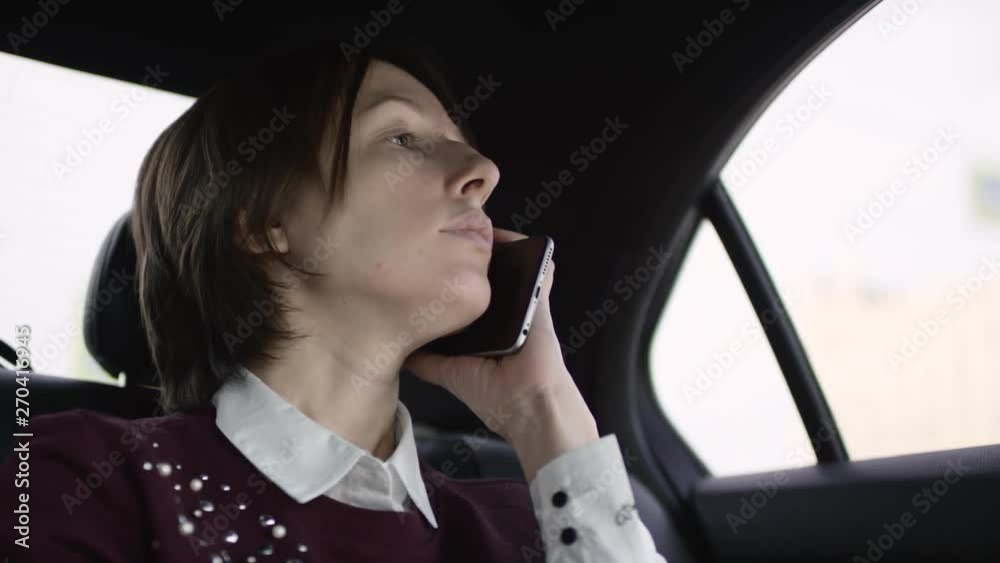 pretty woman with brown hair in white blouse and maroon sweater riding in car and speaking with her phone pretty woman with brown hair in white blouse and maroon sweater riding in car and speaking with her phone
