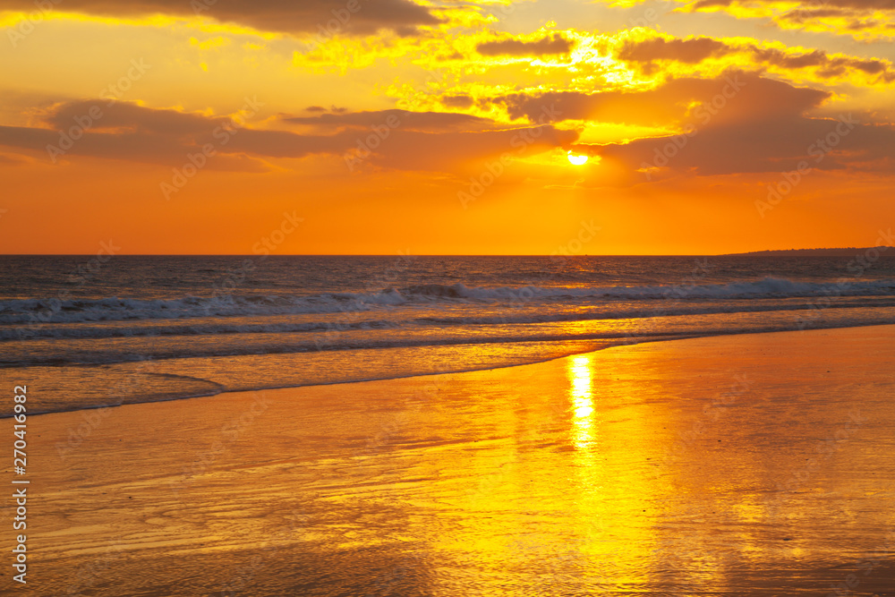 Magnificent sunset on the sea. The rays of the setting sun are reflected in the wet sand. The rich colors of the end of a hot day on the shores of the Atlantic Ocean. Vilamoura, Algarve, Portugal