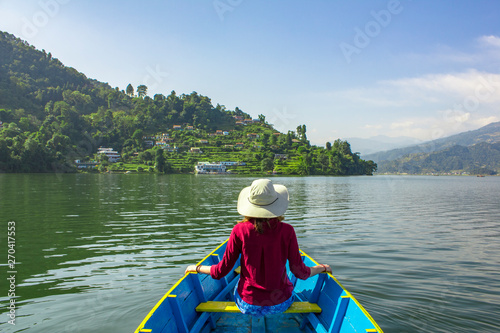 girl in a red shirt and hat in a wooden blue boat on the lake on the background of green mountains