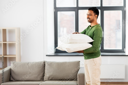 household, housework and cleaning concept - happy indian man holding two pillows or sofa cushion at home