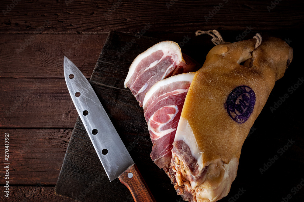 Spanish ham, bellota, jamon serrano, crudo, italian prosciutto, whole leg,  parma ham cut with a knife and lying on a wooden. Top view