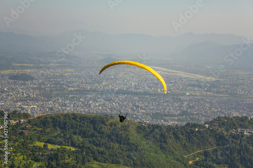 paraglider on a yellow parachute flies against the background of the city in a mountain valley in the fog, aerial view