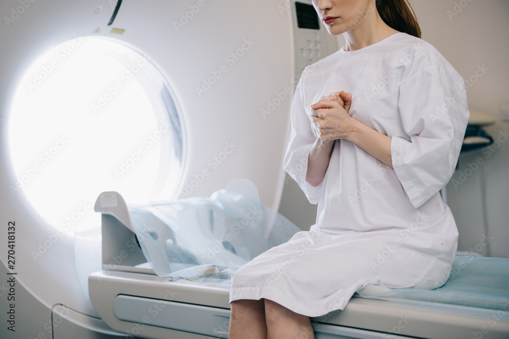 cropped view of woman showing pray gesture while sitting on computed tomography scanner bed cropped view of woman showing pray gesture while sitting on computed tomography scanner bed