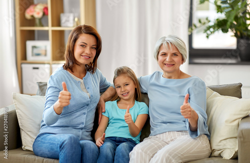 family, generation and female concept - portrait of smiling mother, daughter and grandmother sitting on sofa and showing thumbs up at home