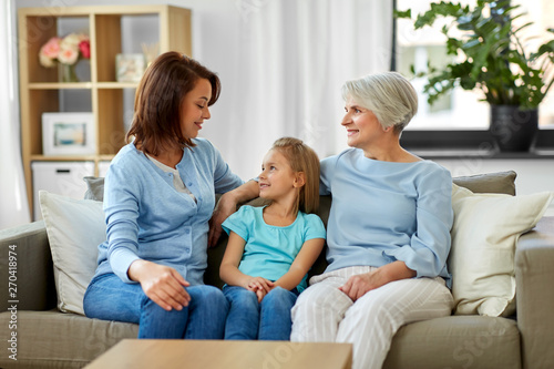 family, generation and female concept - smiling mother, daughter and grandmother sitting on sofa at home