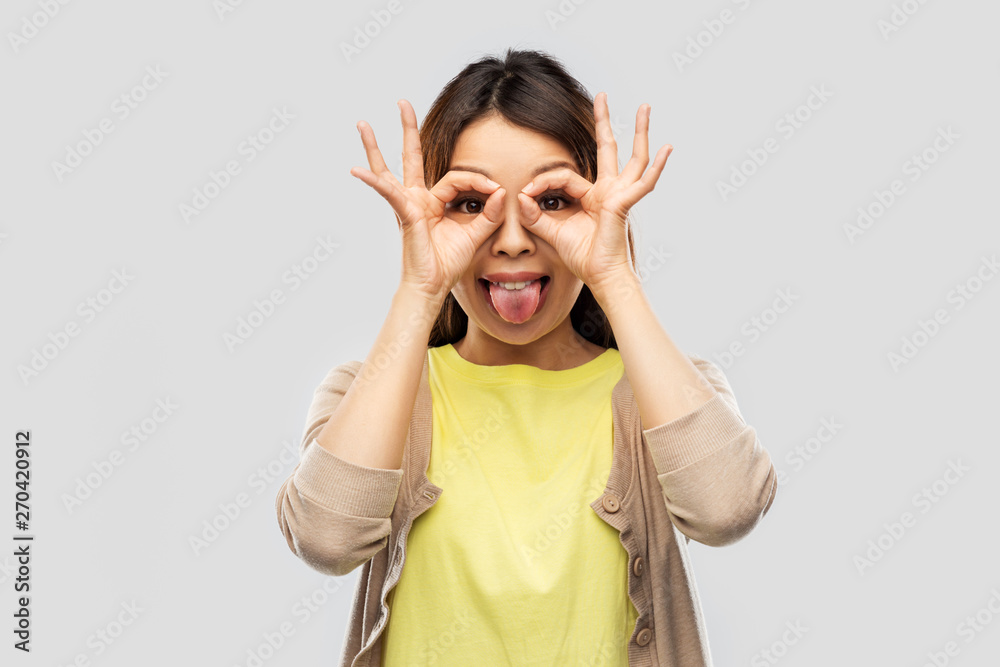 people, gesture and portrait concept - smiling young asian woman looking through finger glasses over grey background people, gesture and portrait concept - smiling young asian woman looking through finger glasses over grey background