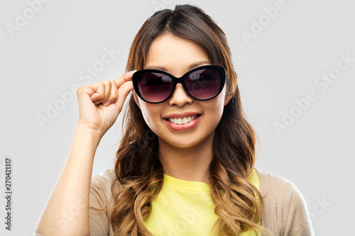 summer fashion, style and eyewear concept - happy smiling young asian woman in sunglasses over grey background