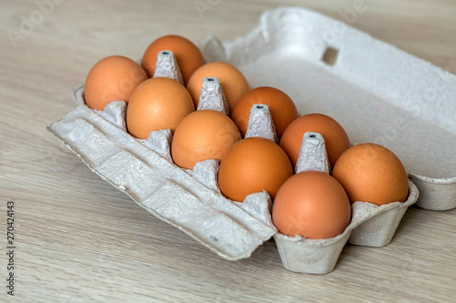Hen eggs in open cardboard egg carton on kitchen table light copy space background. Healthy organic food and diet concept.