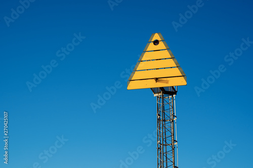 Yellow triangle sign on post in coastal landscape used as landmark orientation for shipping navigation, marine mark