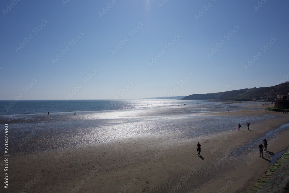 View across beach looking south along cliffs towards sunshine in Scarborough, Yorkshire, UK on a bright blue sky sunny day