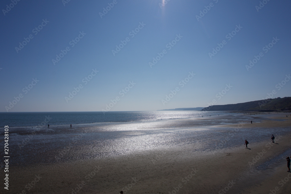 Looking out to sea across empty sandy beach in Scarborough, Yorkshire, UK on a bright bllue sky sunny day