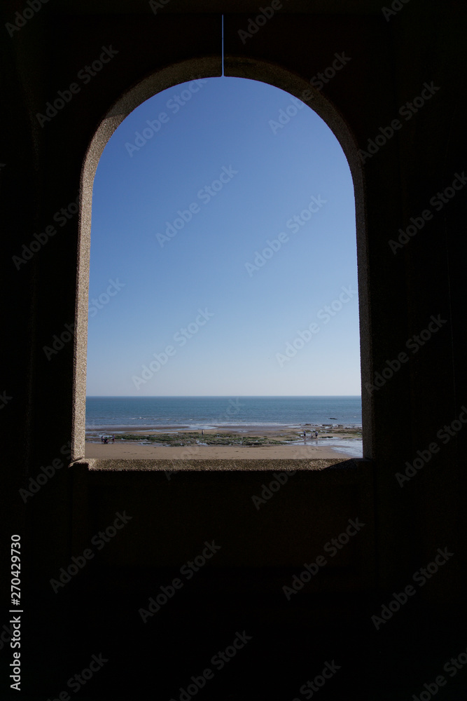 Looking out to sea through archway across empty sandy beach in Scarborough, Yorkshire, UK on a bright blue sky sunny day