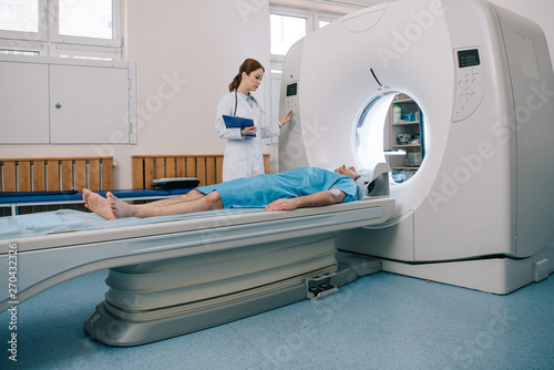 young radiographer operating ct scanner while preparing patient for tomography photo