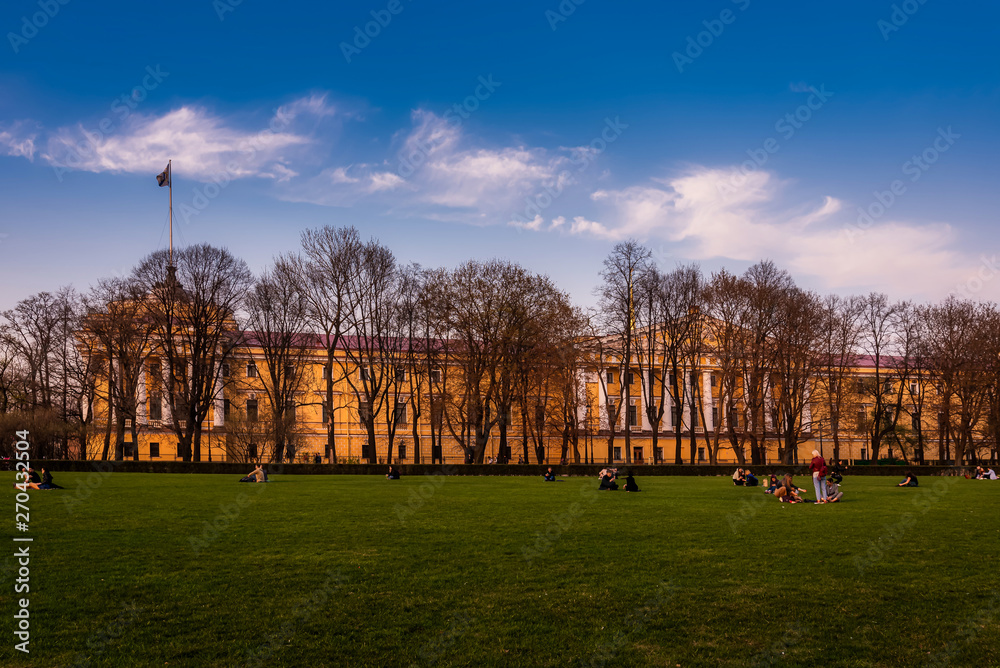Obraz premium People rest on the meadow of the Alexander Garden with the Admiralty Building in the background at dawn in Saint Petersburg, Russia